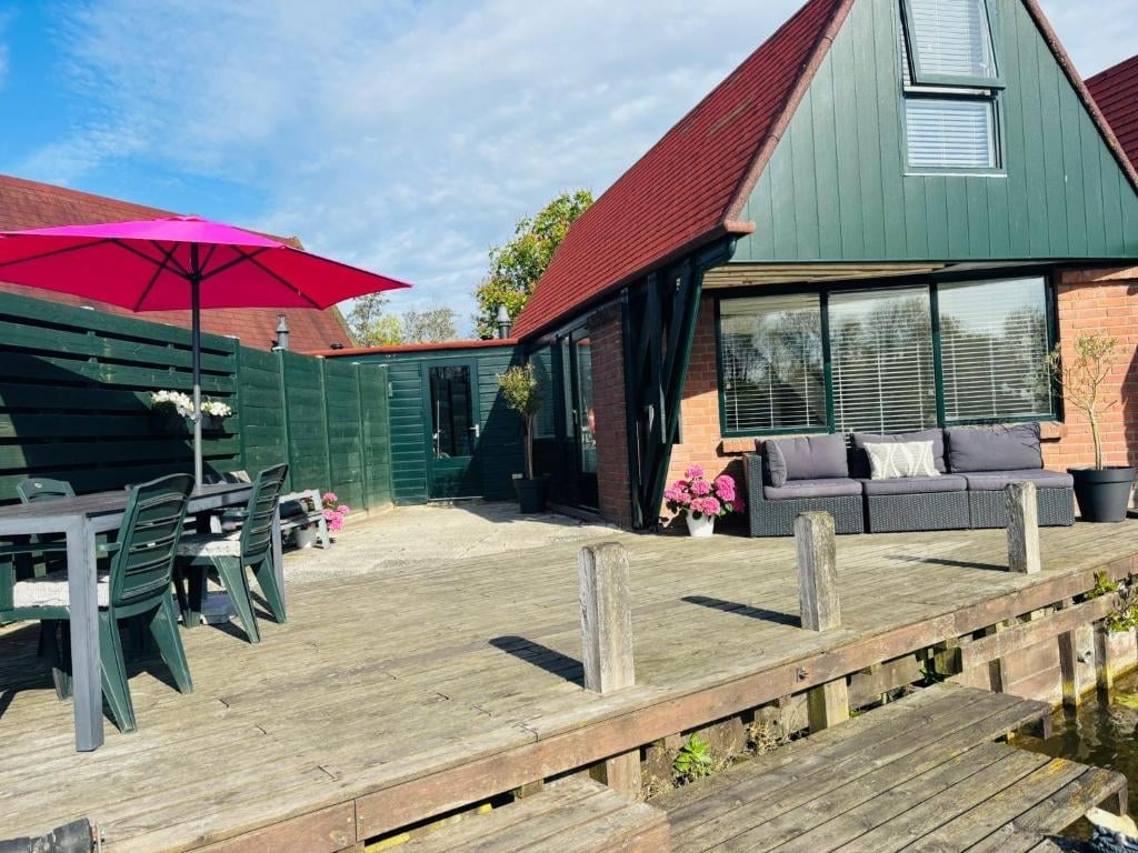 Modern cottage with red umbrella on wooden patio, brick building with green roof and large windows