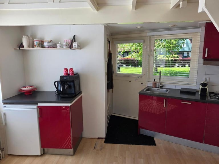 Modern kitchen with red and white cabinets, coffee maker, and French doors opening to backyard view