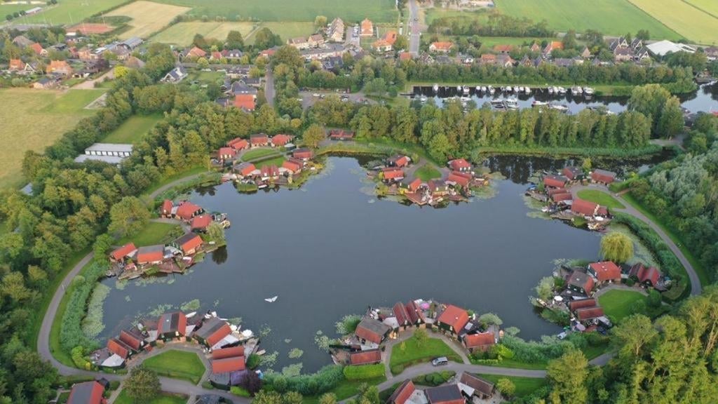 Aerial view of a lakeside residential community with red-roofed houses surrounding a central lake, surrounded by green fields and forests