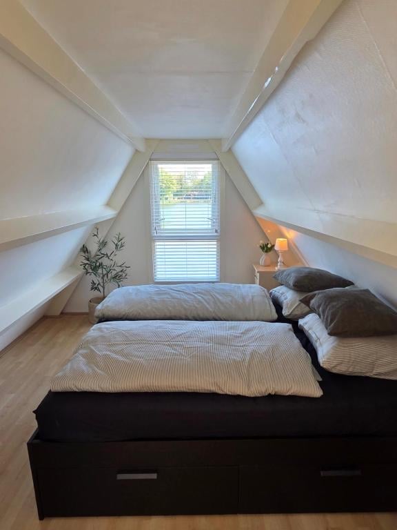 Cozy attic bedroom with sloped ceilings, a bed with striped bedding, a window with shutters, and minimal furnishings including a small plant and lamp