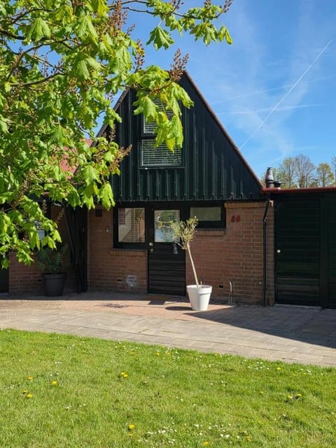 Modern brick and black converted barn building with triangular roof, large windows, small tree in pot, brick patio, and green lawn in front on sunny day